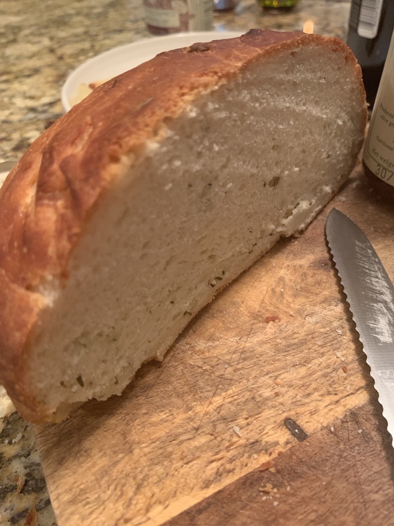 Loaf of homemade bread cut in half on a cutting board and serrated knife.